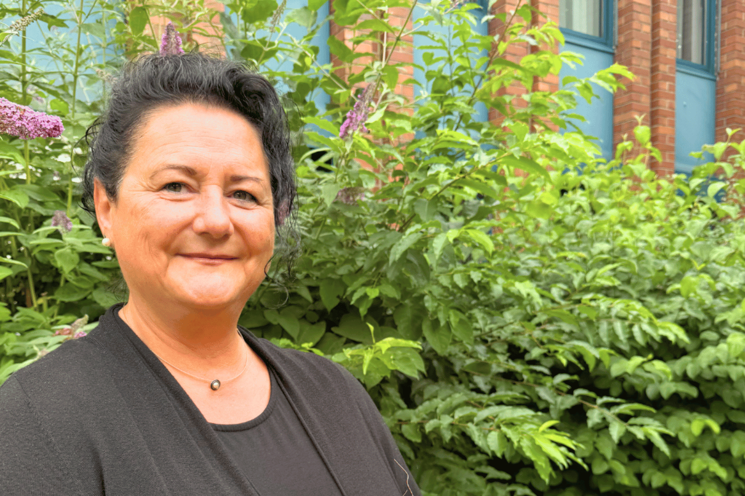 Eine Frau in schwarzer Bekleidung blickt lächelnd in die Kamera