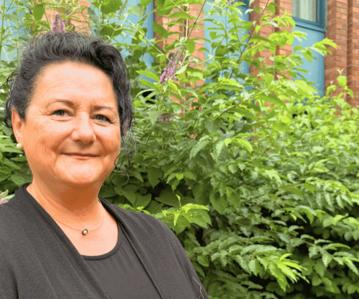 Eine Frau in schwarzer Bekleidung blickt lächelnd in die Kamera