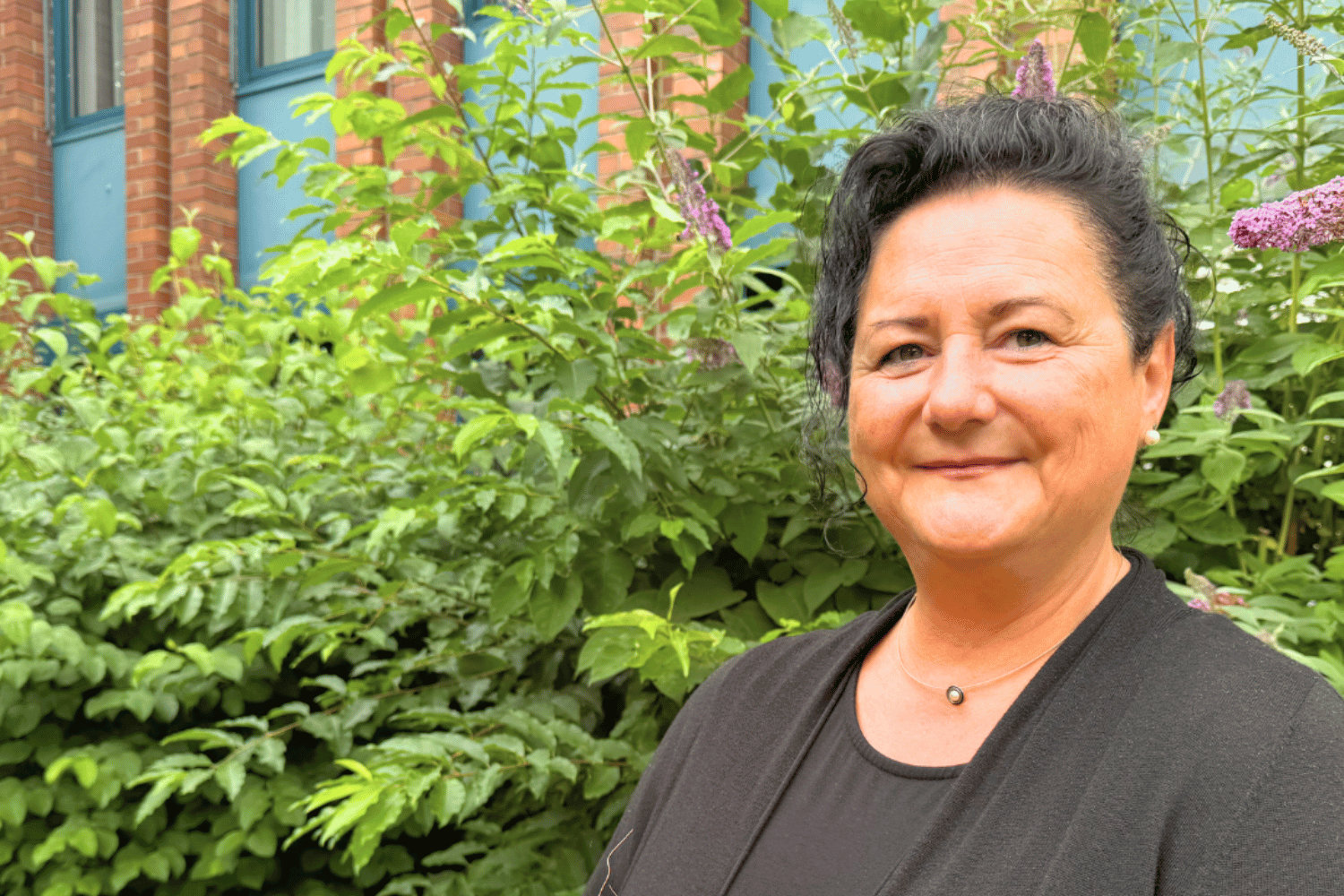 Eine Frau in schwarzer Bekleidung blickt lächelnd in die Kamera