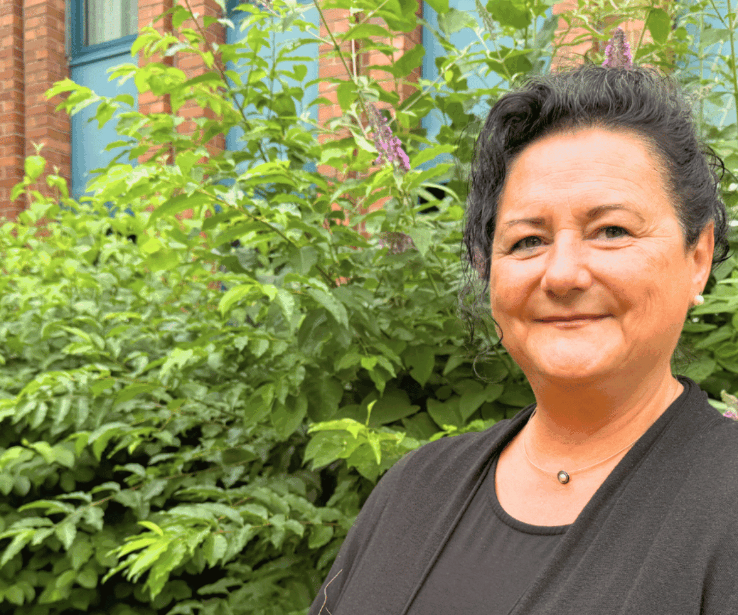 Eine Frau in schwarzer Bekleidung blickt lächelnd in die Kamera