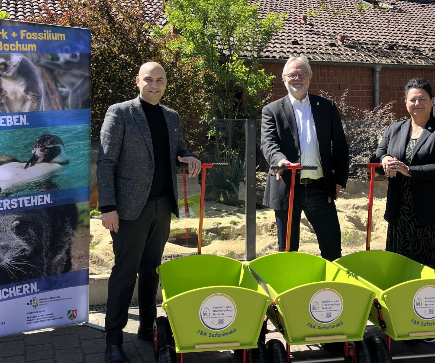 3 Personen stehen mit grünen Bollerwagen bei Sonnenschein im Bild.